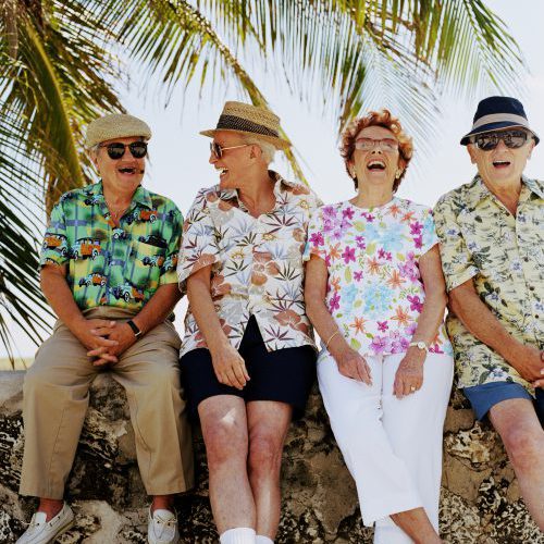 Group of four senior people sitting on wall outdoors, laughing