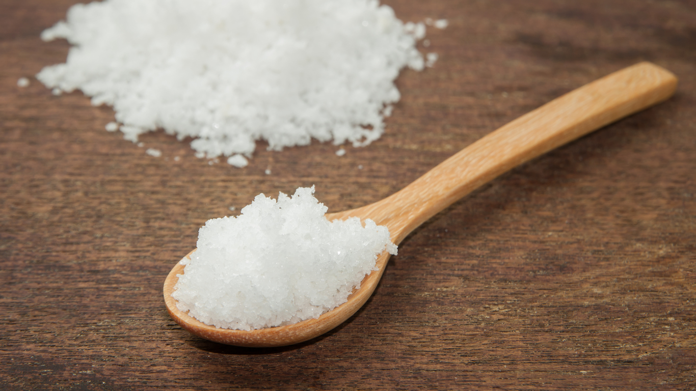 salt in wood spoon on wooden background .