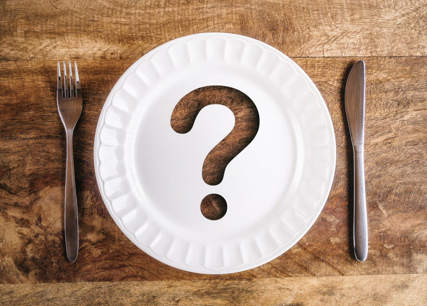 Question mark on plate with fork and knife on rustic wooden table in natural light, top view