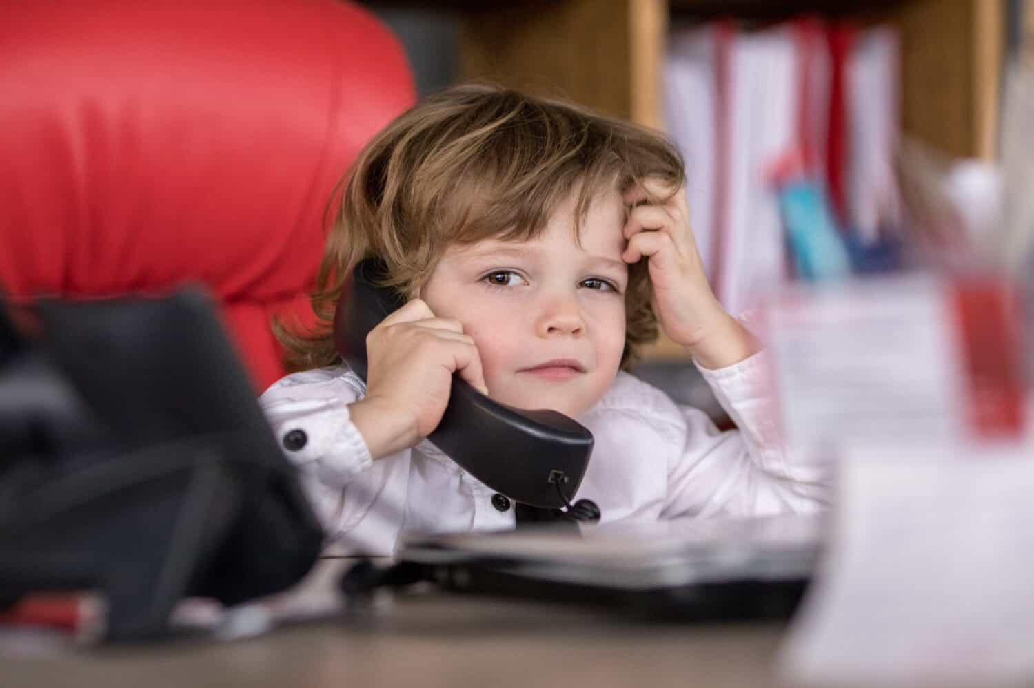 Little boy sits in the office in the chair and talking on the phone. Little boss.