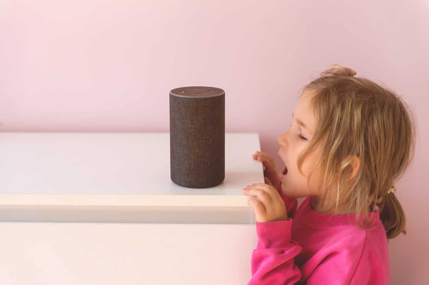 Little kid girl talking to talking to Amazon Alexa Echo Dot. Education programme for child. kid girl talking to Alexa and give it orders and commands what to switch on.