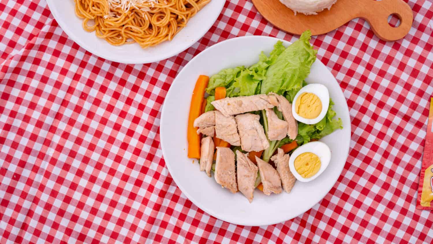 Red checked tablecloth picnic with spaghetti, chicken egg salad, vietnam coffee and cake with wooden spoon and white plate