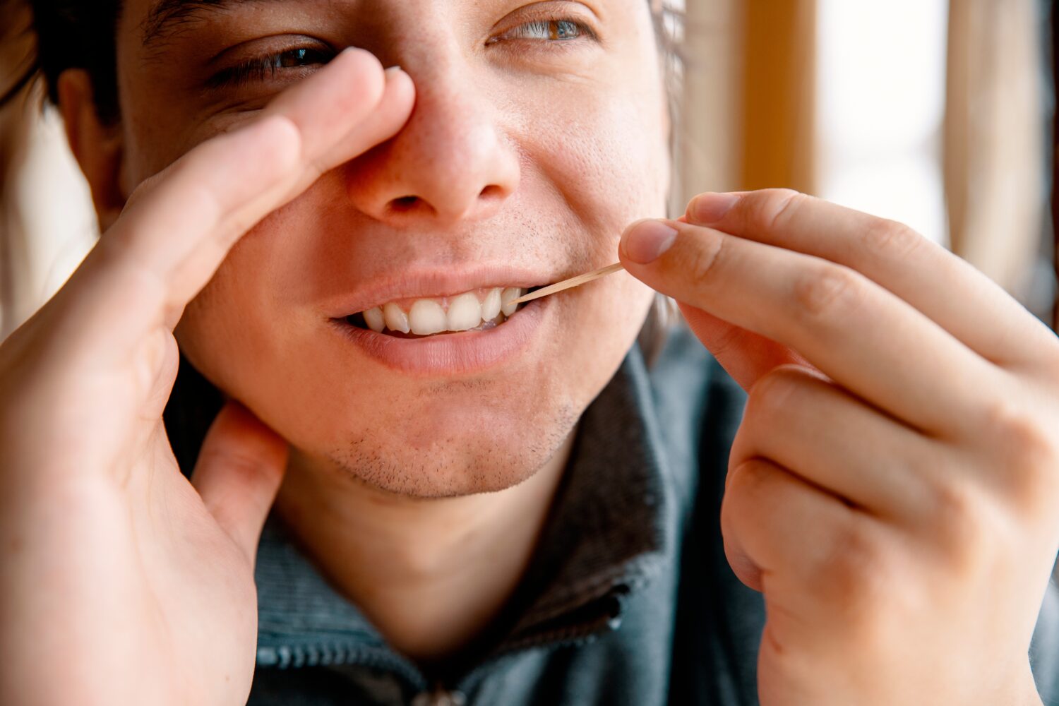 Man Cleaning teeth with a toothpick hiding mouth with hand. Male using Disposable Double-end Teeth Stick Floss Pick to clean teeth. Toothpick Dental Brush Oral Care concept