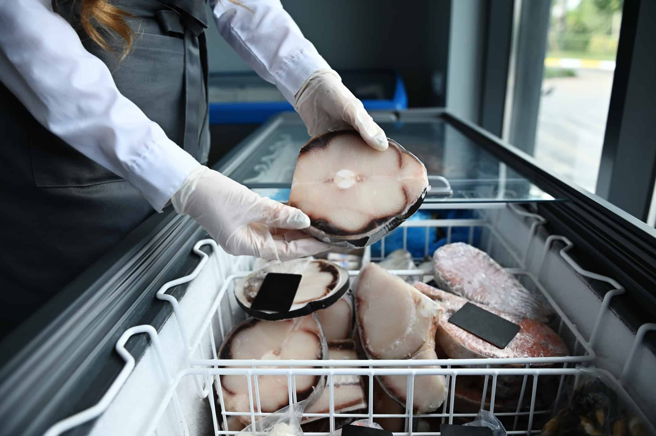 Fishmonger holding a piece of frozen sea shark fillet. A fish vendor in a seafood market taking a frozen fish steak out of the refrigerator