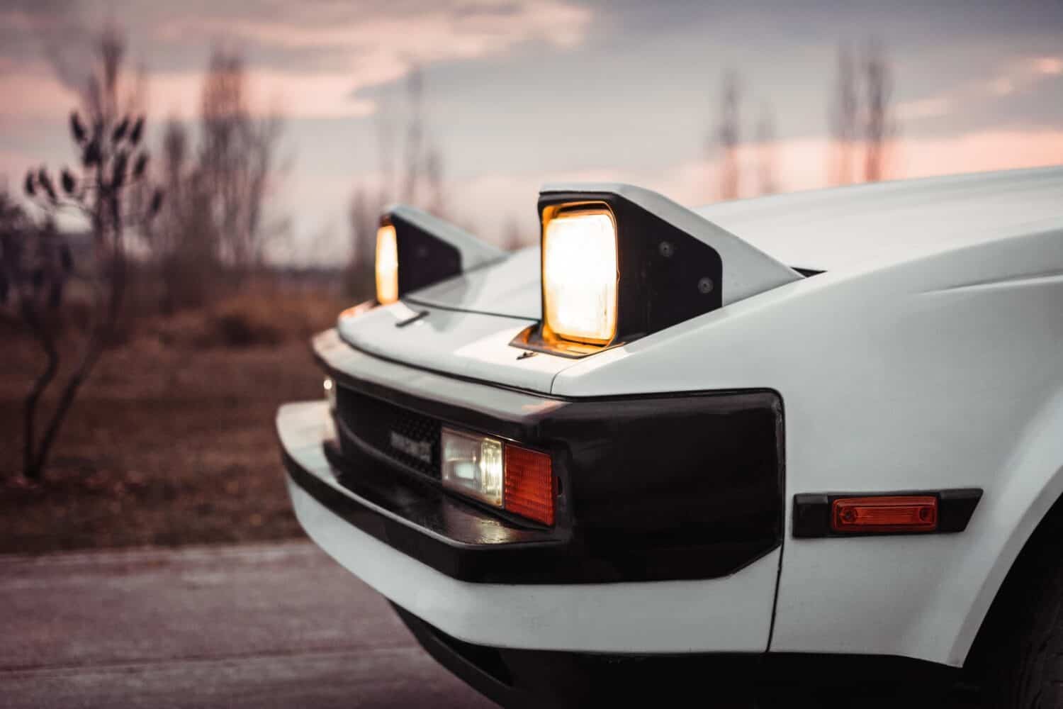 White old japanese 1980s car with pop-up headlights. Blurry countryside in the background