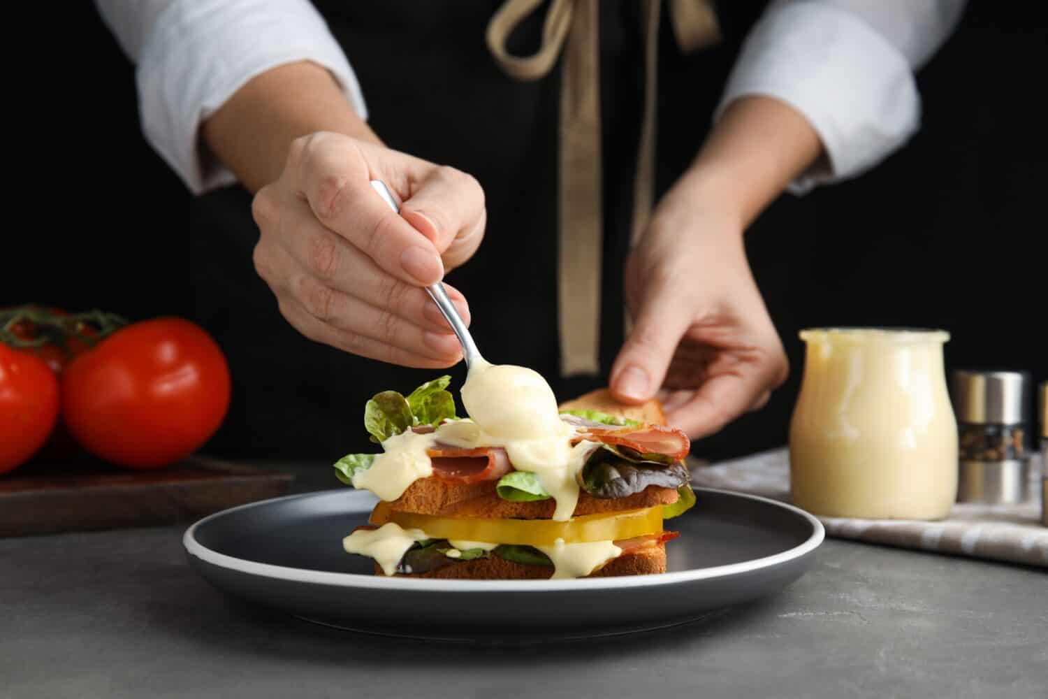 Woman making sandwich with mayonnaise at grey table, closeup