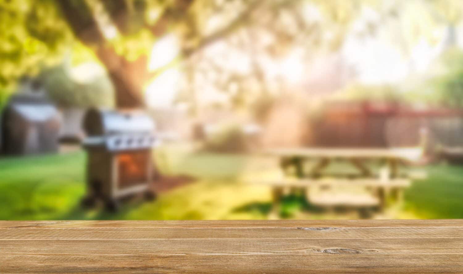 summer time in backyard garden with grill BBQ, wooden table, blurred background