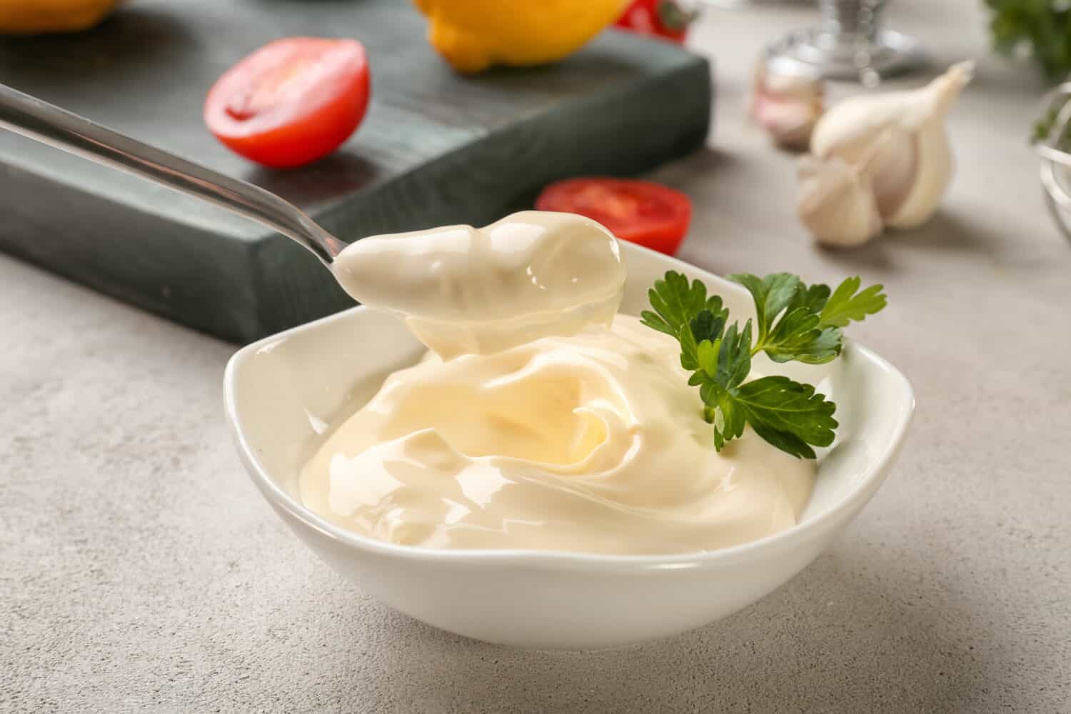 Delicious mayonnaise in bowl and spoon on kitchen table, closeup