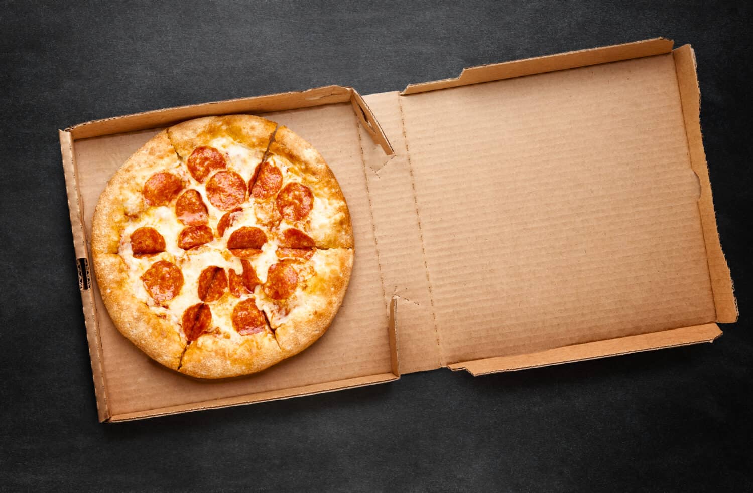 Pizza in a cardboard box on a dark chalkboard. Space for your text. Top view of pizza package. Pizza delivery.