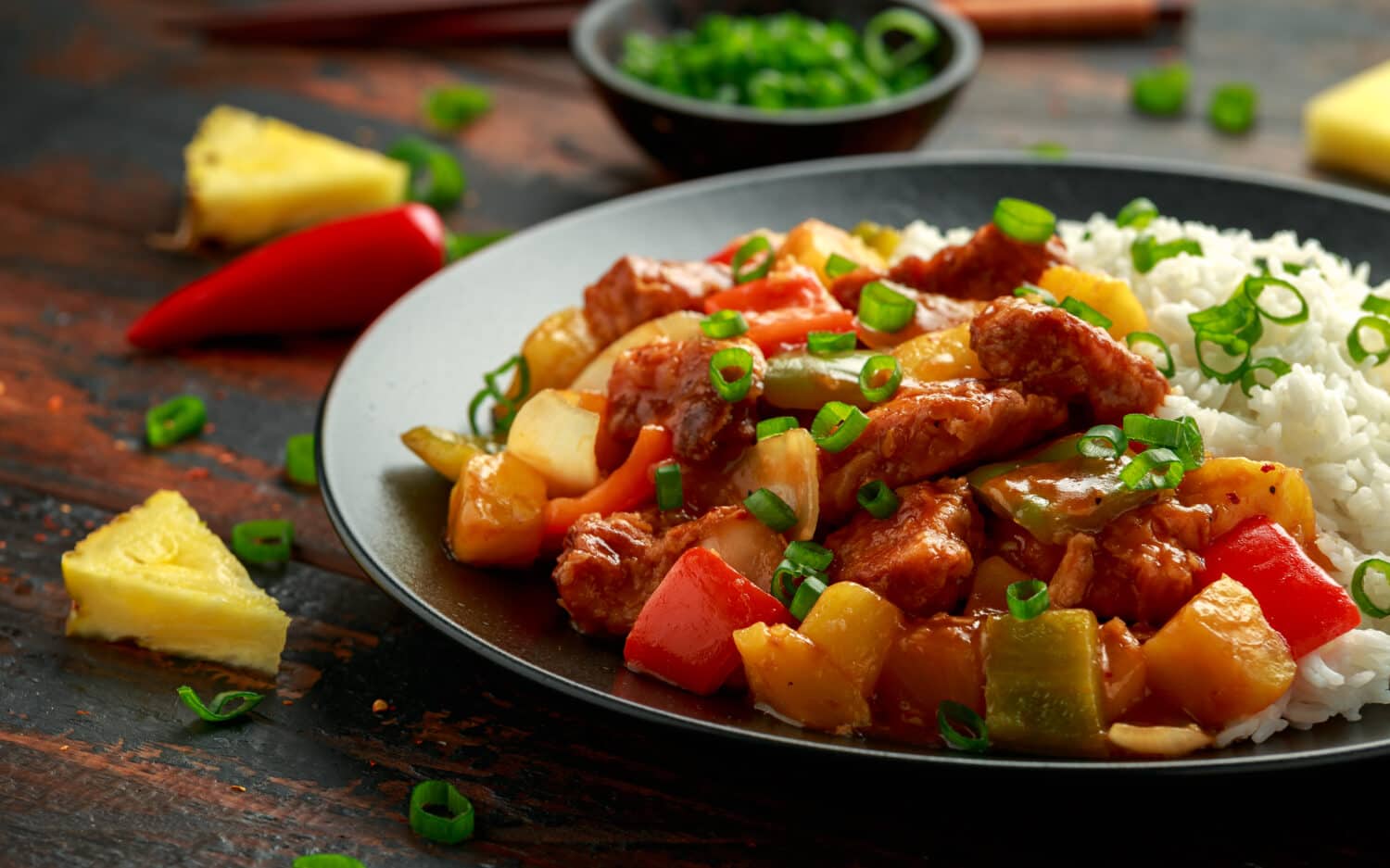 Pineapple and Chicken in sweet and sour sauce with bell pepper, rice and spring onion in black plate