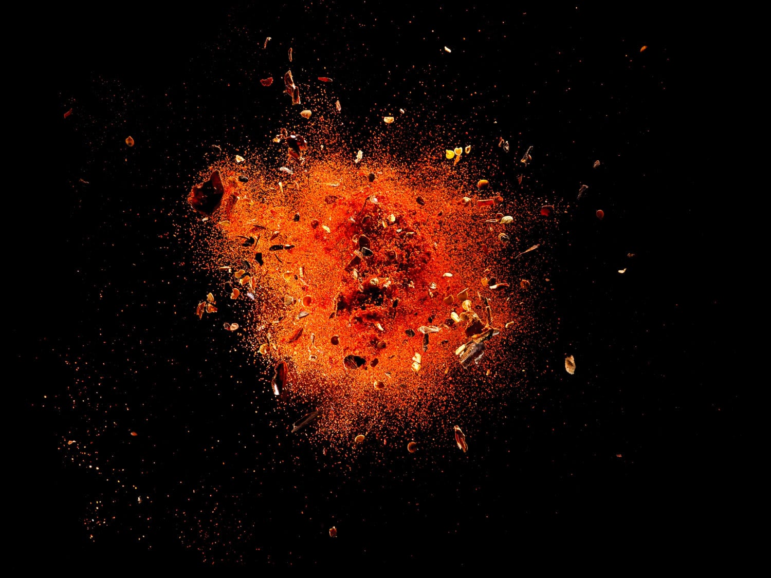 Explosion of red cayenne pepper with flakes and seeds on black background