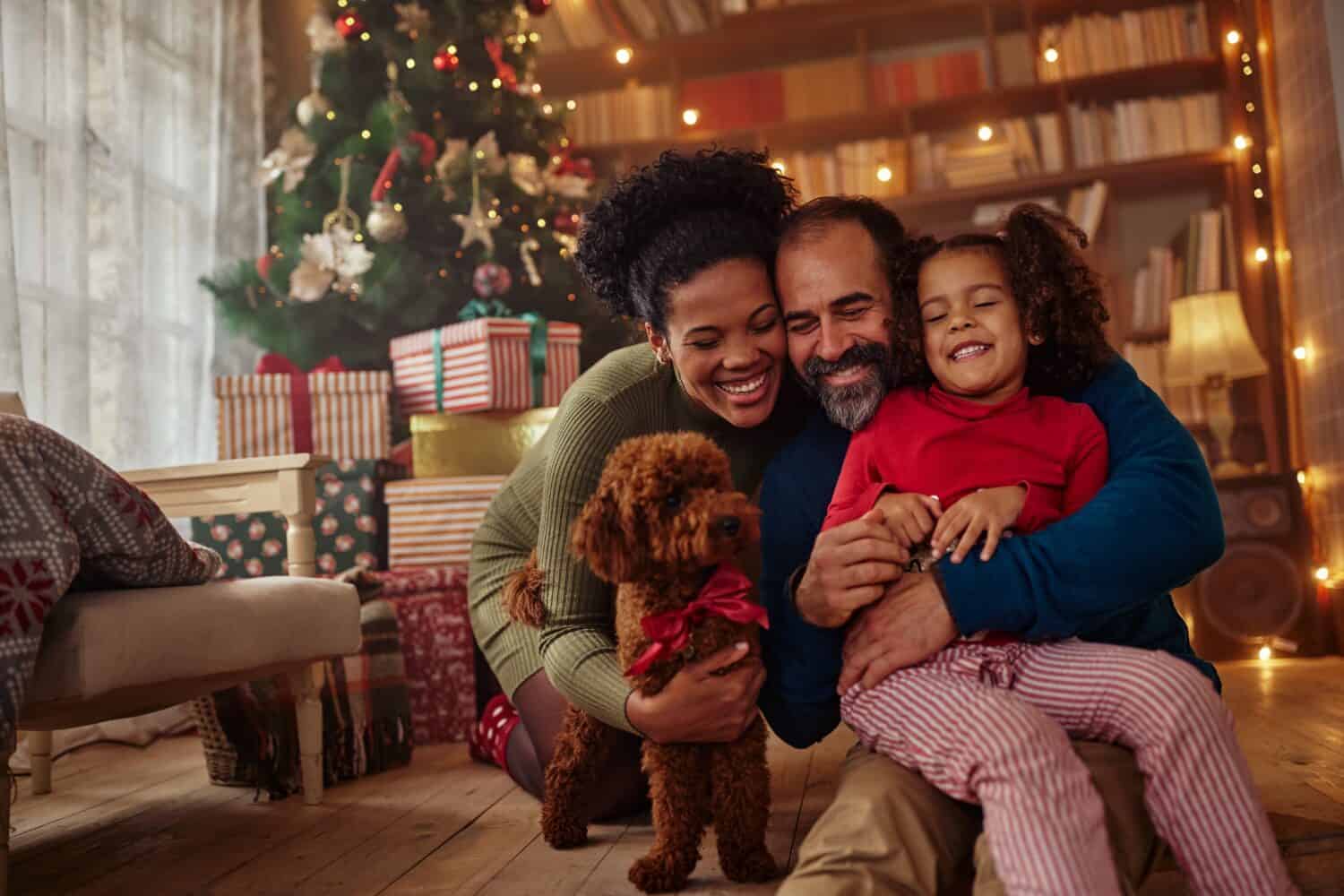 Excited girl and her family sitting on the floor near christmas tree and smiling. Mixed race family during Christmastime