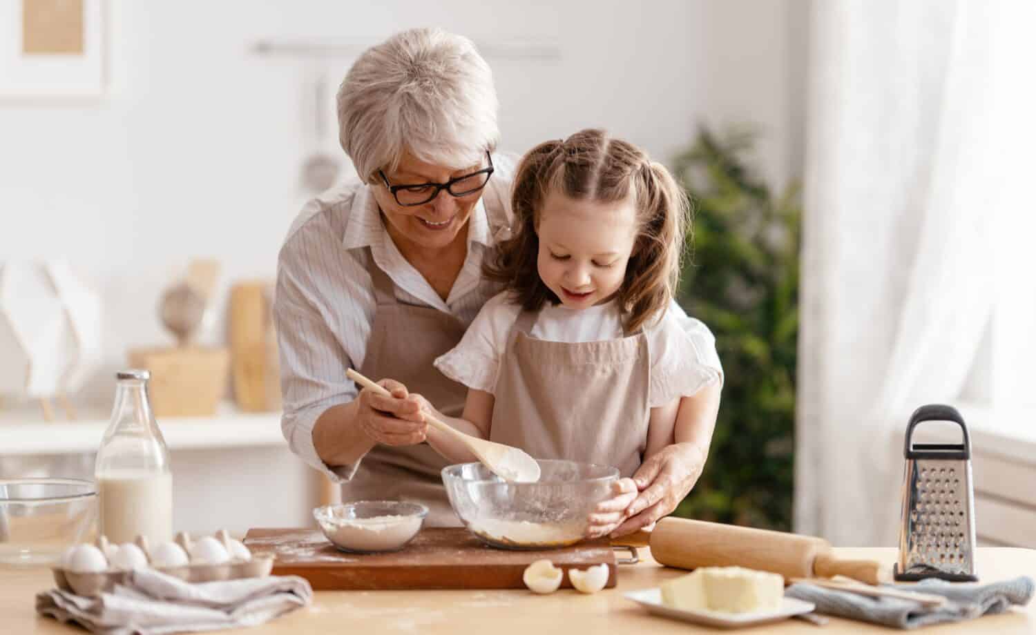 Happy loving family are preparing bakery together. Granny and child are cooking cookies and having fun in the kitchen.