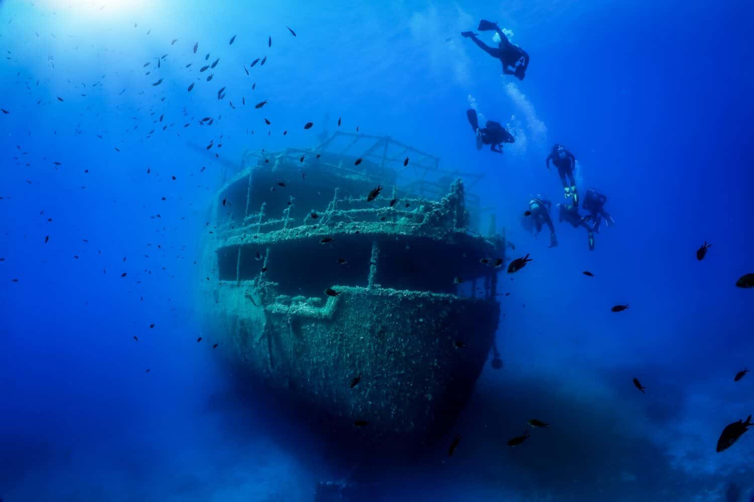 A group of unrecognizable divers explore a sunken shipwreck in the blue, mediterranean sea at Naxos island, Greece