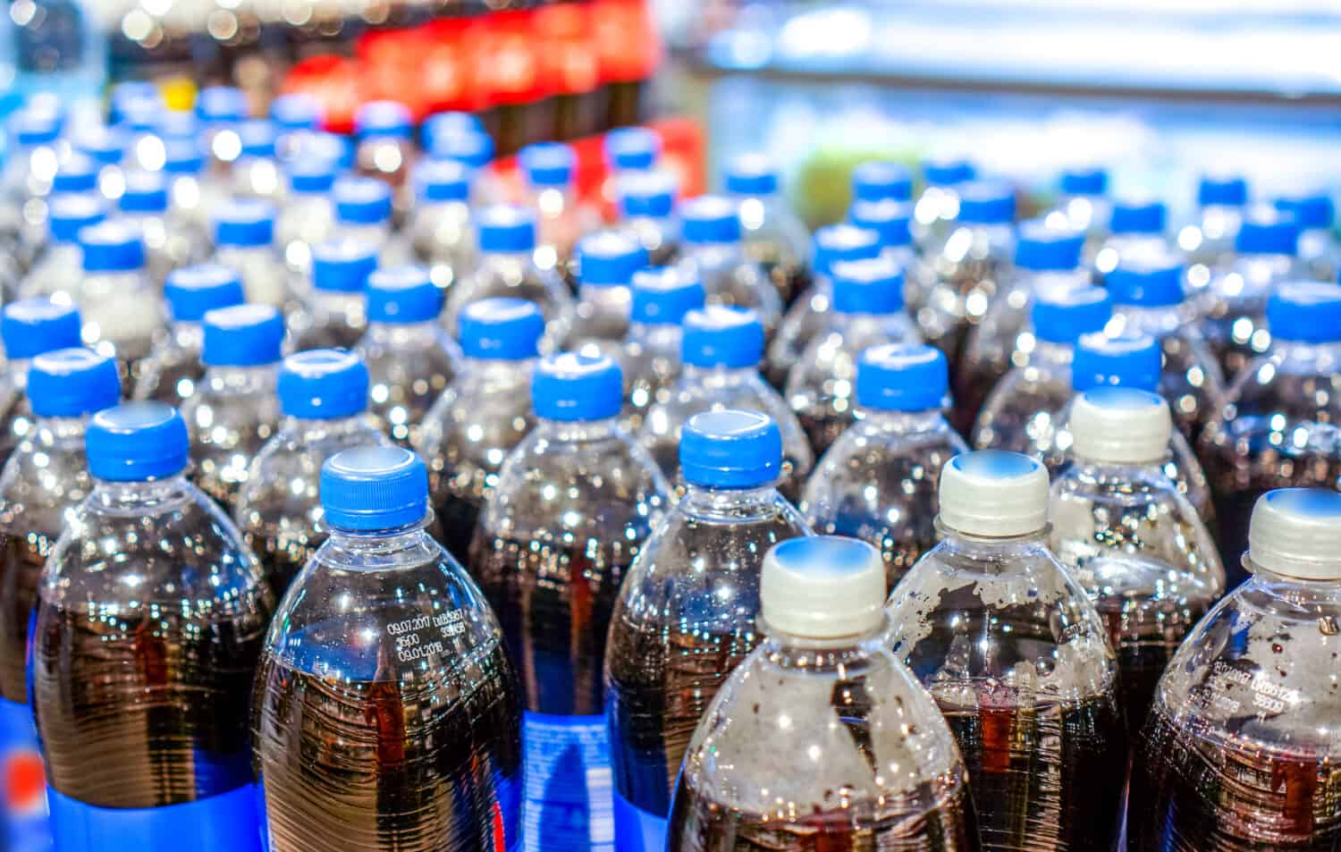 army of plastic bottles with black liquid and navy blue covers stand in strong rows at shop and wait for buyers. Many bottles with pepsi top view. background made by big pepsi bottles