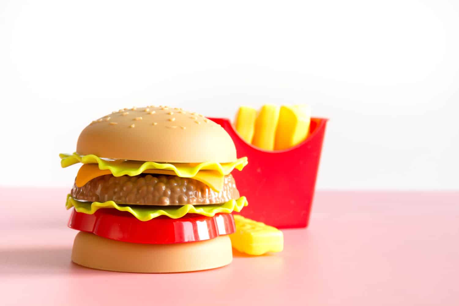 Plastic burger, salad, tomato, frying potato with on pink background. Horizontal orientation. Children&#039;s toy. Concept of harmful artificial food. Plastic. Not organic. Not useful.