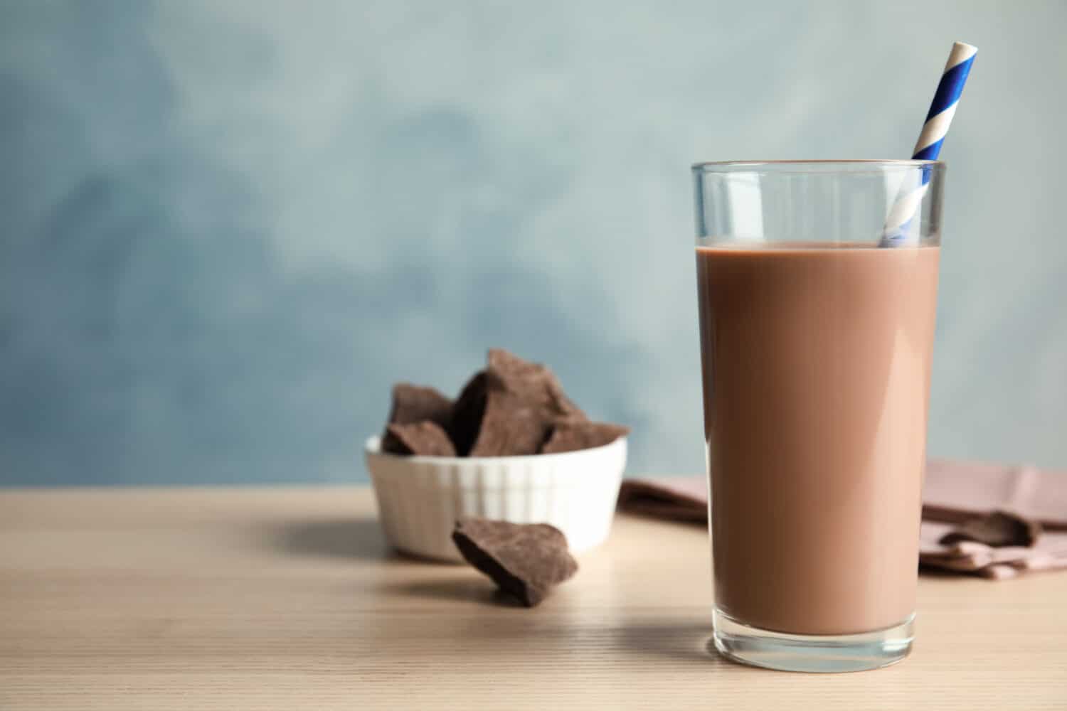 Glass of tasty chocolate milk on wooden table, space for text. Dairy drink