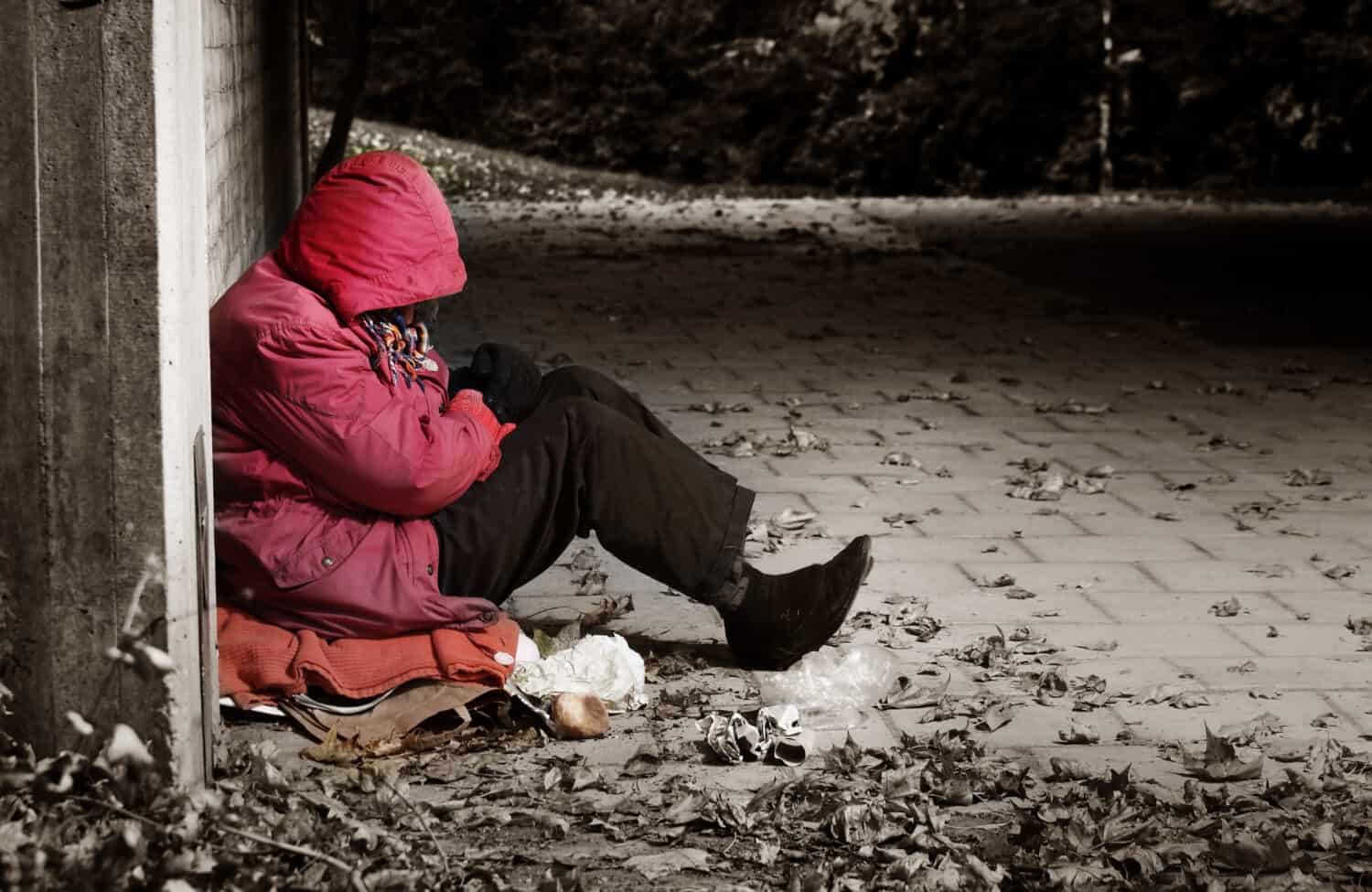 A woman sitting against a brick building with her head in her arms