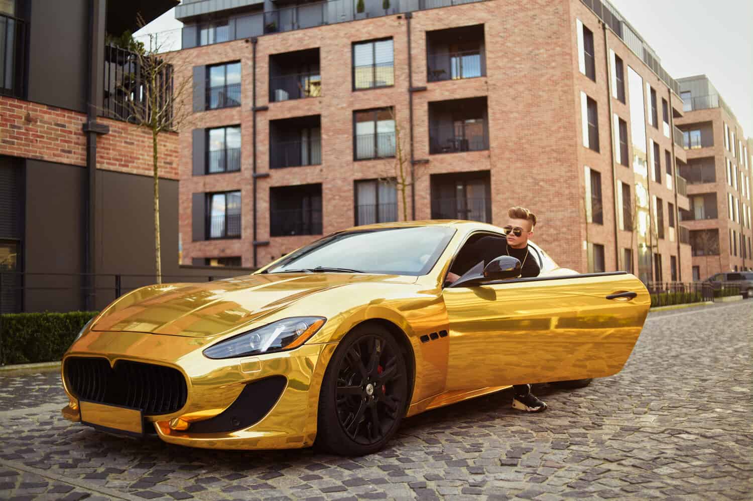 A businessman is sitting in a golden car. A man is driving inside a car. Driver. Chic man with glasses, with a perfect haircut, glasses, fashionable. Freelancer. Rich boy. A teenager drives a car.