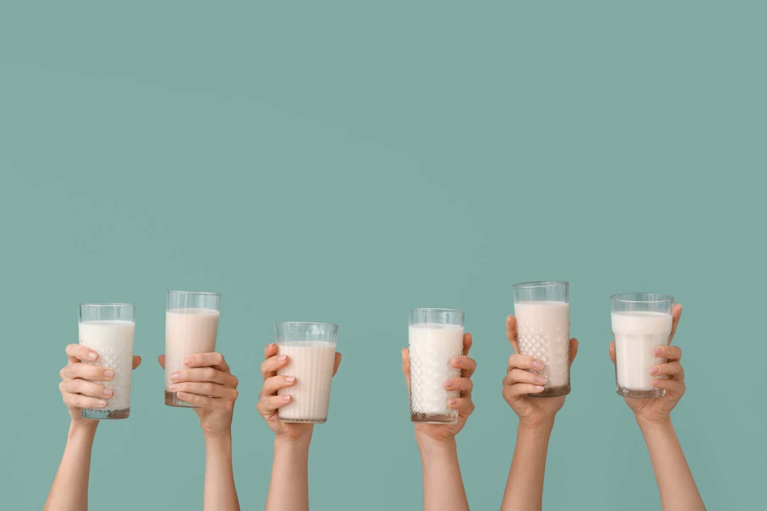 Female hands with glasses of vegan milk on color background