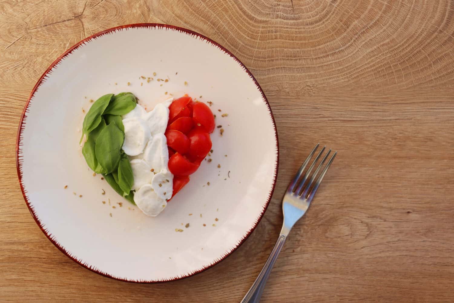 Heart shaped Italian Caprese Salad arranged by Italian basil,buffalo mozzarella and tomatoes look like Italian Flag on plate with wooden table background.Love Italian food concept for Valentine day