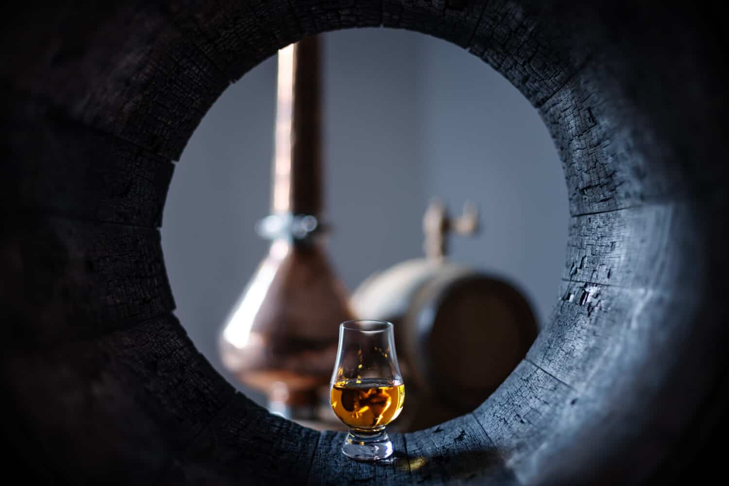 A glass of whiskey in old oak barrel. Copper alambic on background. Traditional alcohol distillery concept