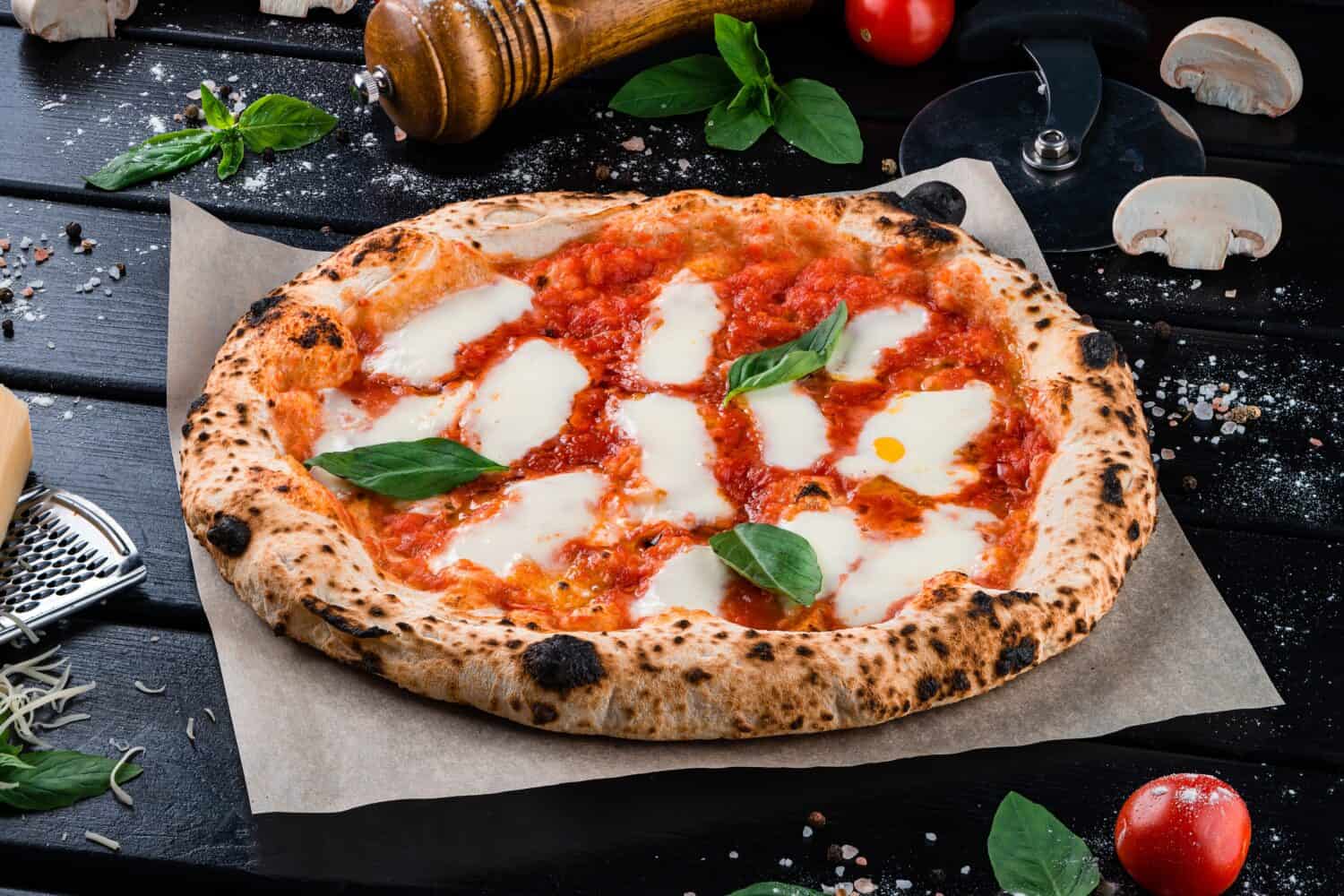 Neapolitan pizza with spices, tomatoes and cheese mozzarella on dark background. Pizza with mozzarella, tomato sauce, spinach on a thick dough.