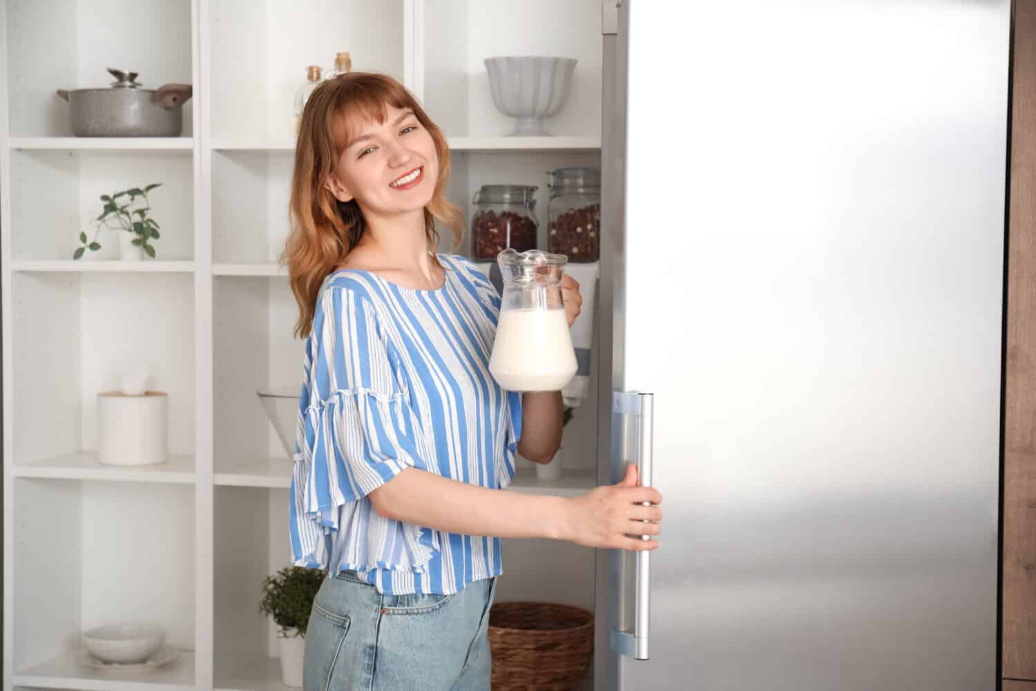 Young woman with jug of milk near fridge in kitchen