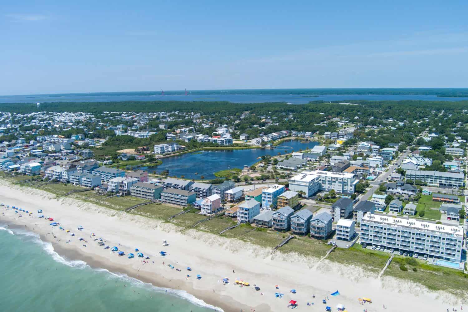 aerial shot of the coastline with green ocean water, waves, people on the beach, homes along the shore, Carolina Lake and lush green trees and grass in Carolina Beach North Carolina USA