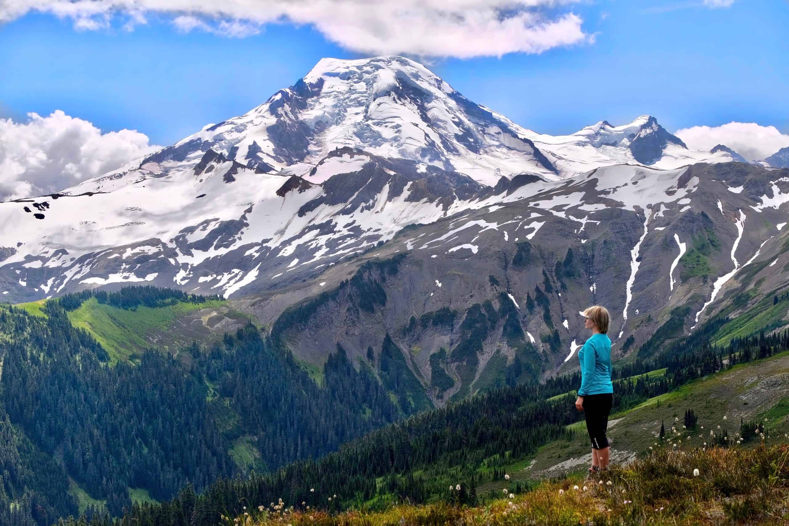 Bellingham, WA people | Sporty woman relaxing in alpine meadows and enjoying scenic view of volcano covered with glaciers and snow.