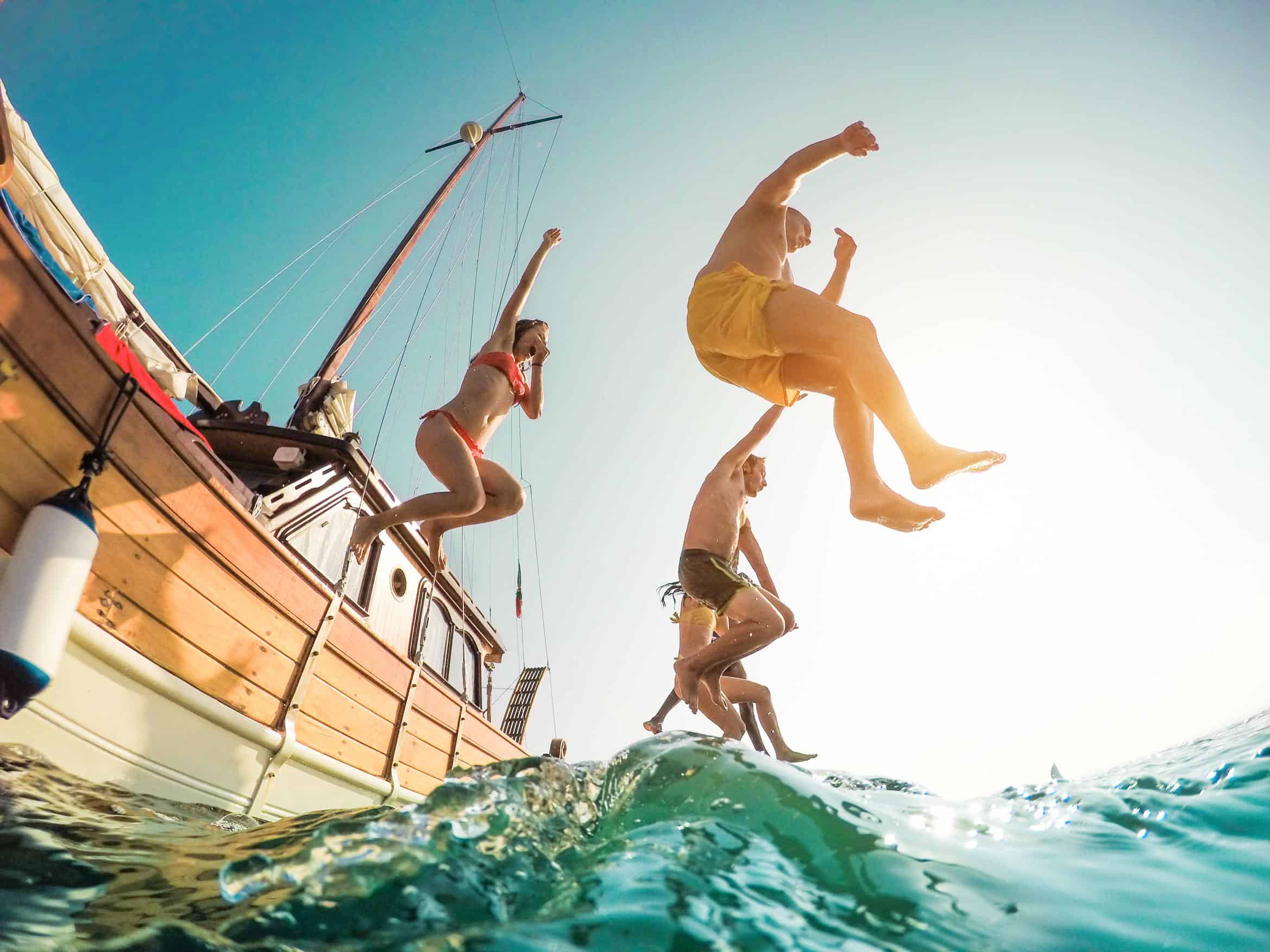 Miami people | Happy friends diving from sailing boat into the sea - Young people jumping inside ocean in summer excursion day - Vacation, youth and fun concept - Main focus on left man - Fisheye lens distortion