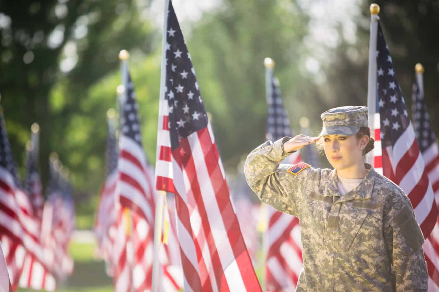 Hispanic American Female Soldier in uniform saluting in front of American flags