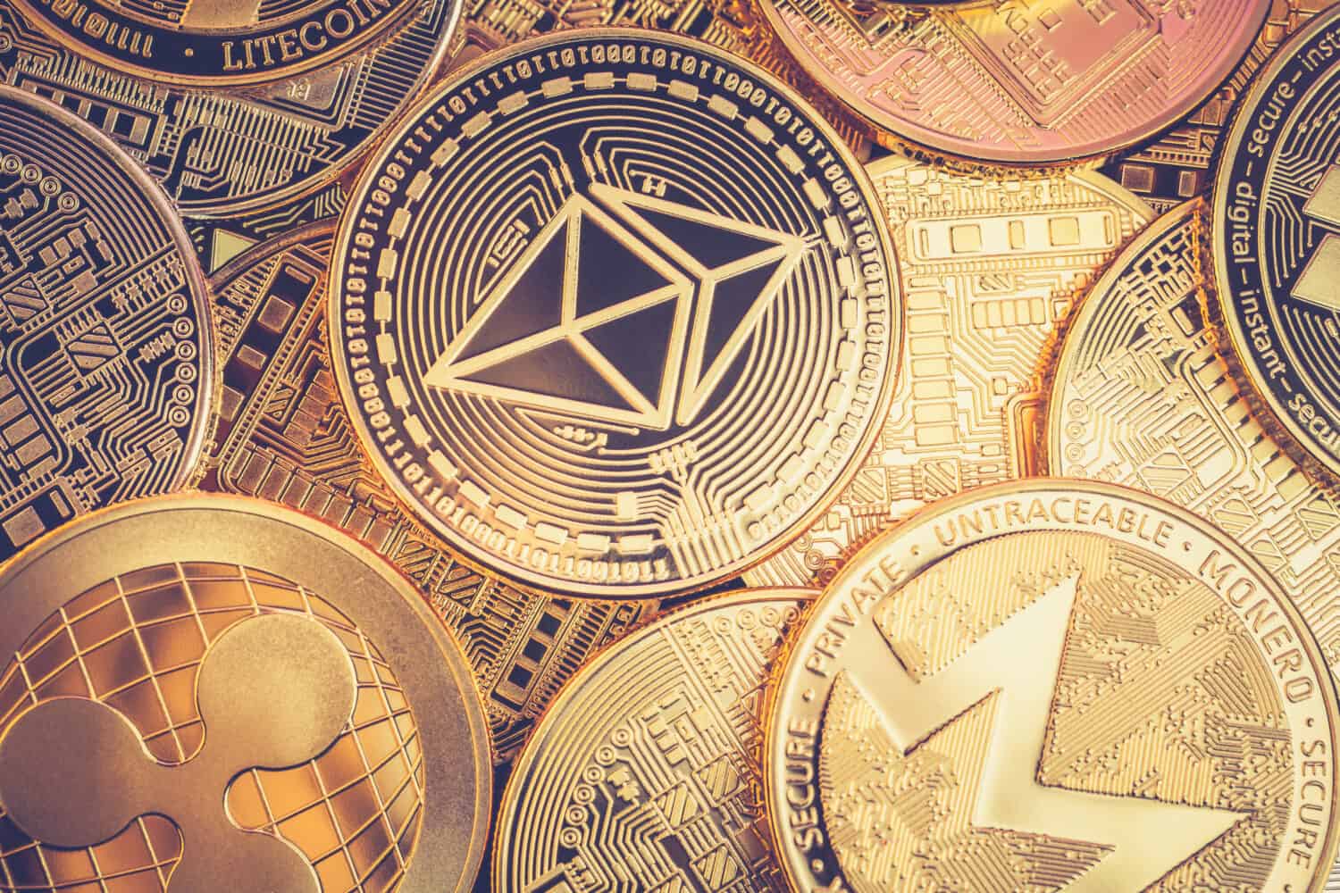 A heap of Ethereum (ETH) physical golden and shiny coins along with different other cryptocurrencies (monero, ripple) with a vintage look. Ethereum is a digital blockchain cryptocurrency