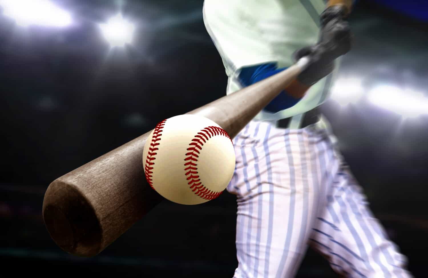 Baseball player hitting ball with bat in close up under stadium spotlights