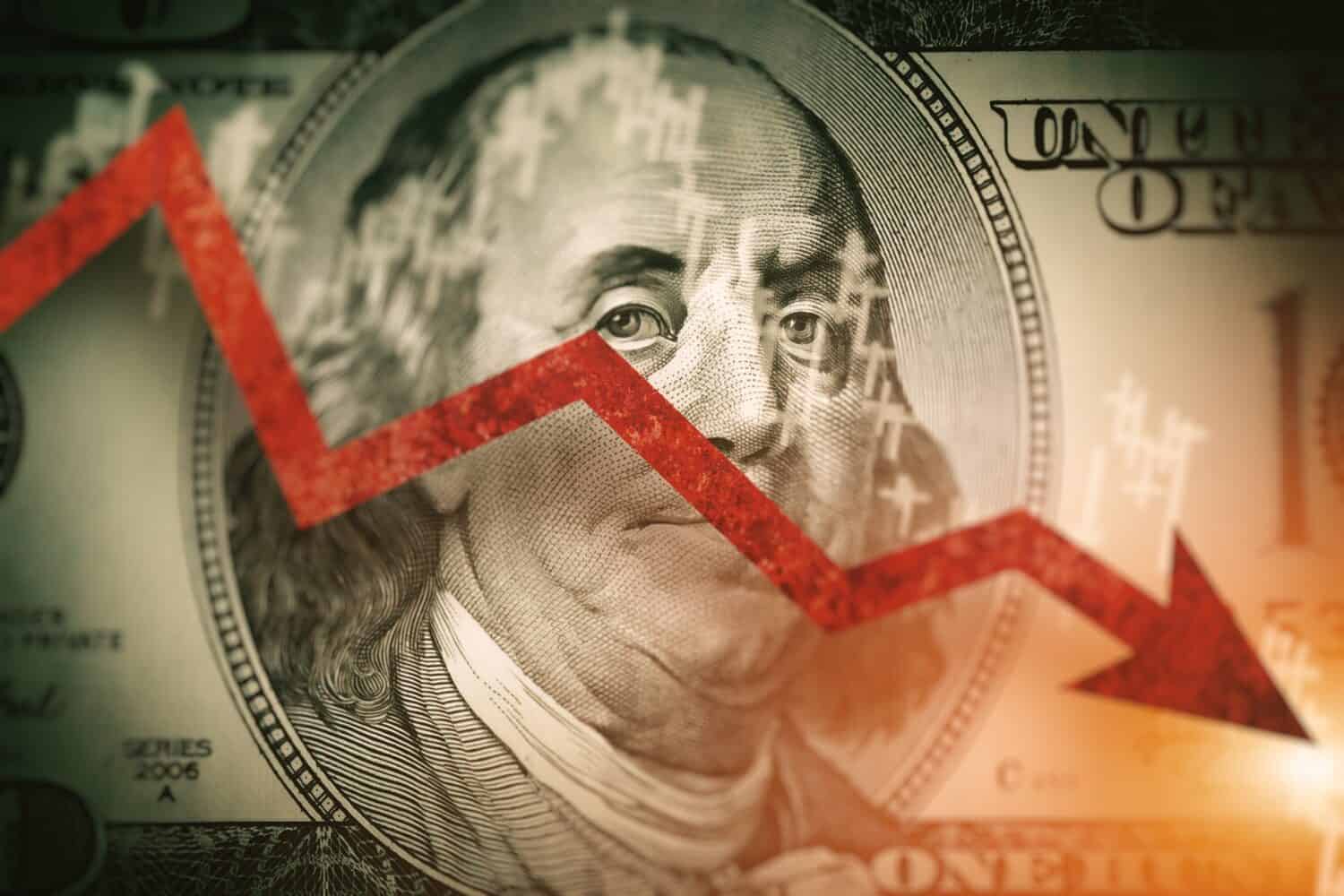 Closeup detail of dollar bill. Economist forecast for the United States. Glowing red arrow going downwards on Benjamin Franklin portrait on dollar bill. Effect of recession on US economy.