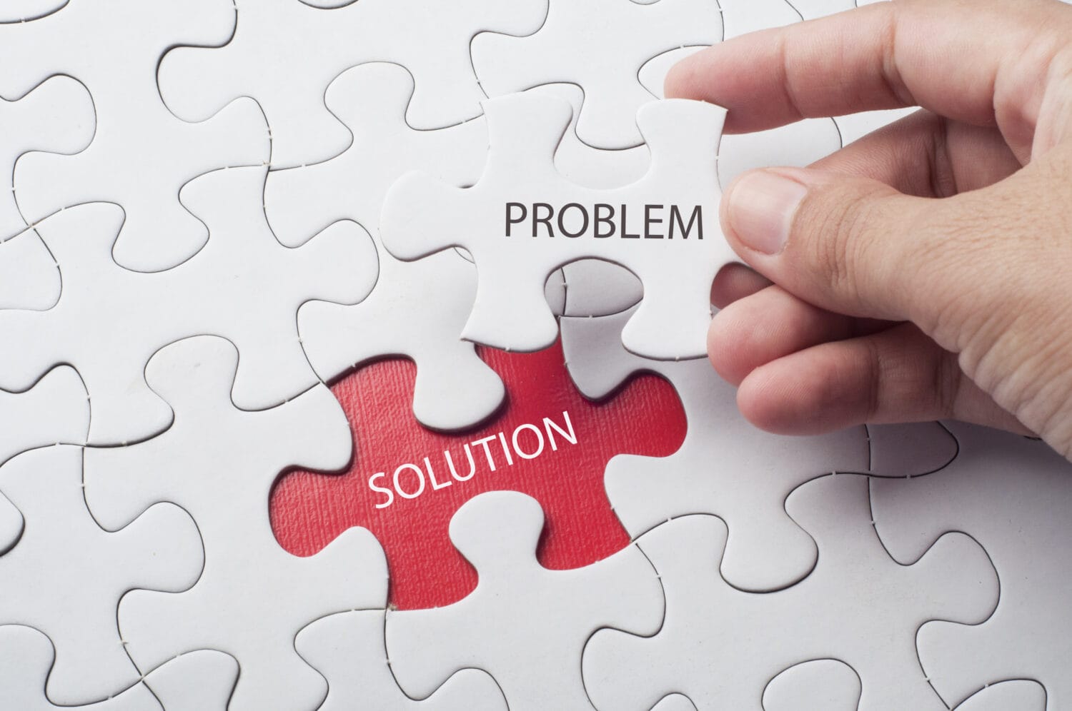 Hand holding piece of jigsaw puzzle with word problem &amp; solution.