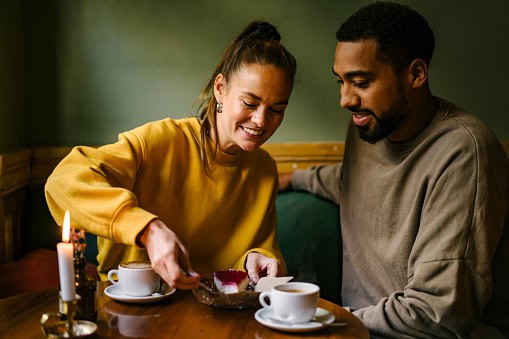 Female enjoying raspberry dessert while boyfriend watches