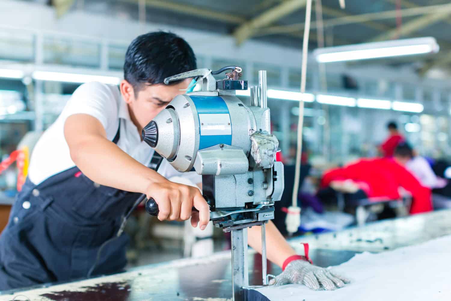 Indonesian worker using a cutter - a large machine for cutting fabrics - in a asian textile factory, he wears a chain glove