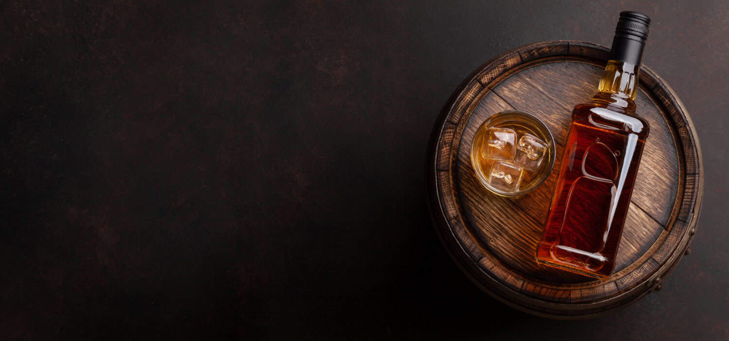 Scotch whiskey bottle, glass and old wooden barrel. With copy space. Top view flat lay