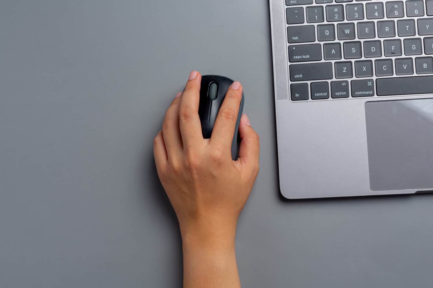 woman works with a laptop at home and holds a computer mouse in her left hand.