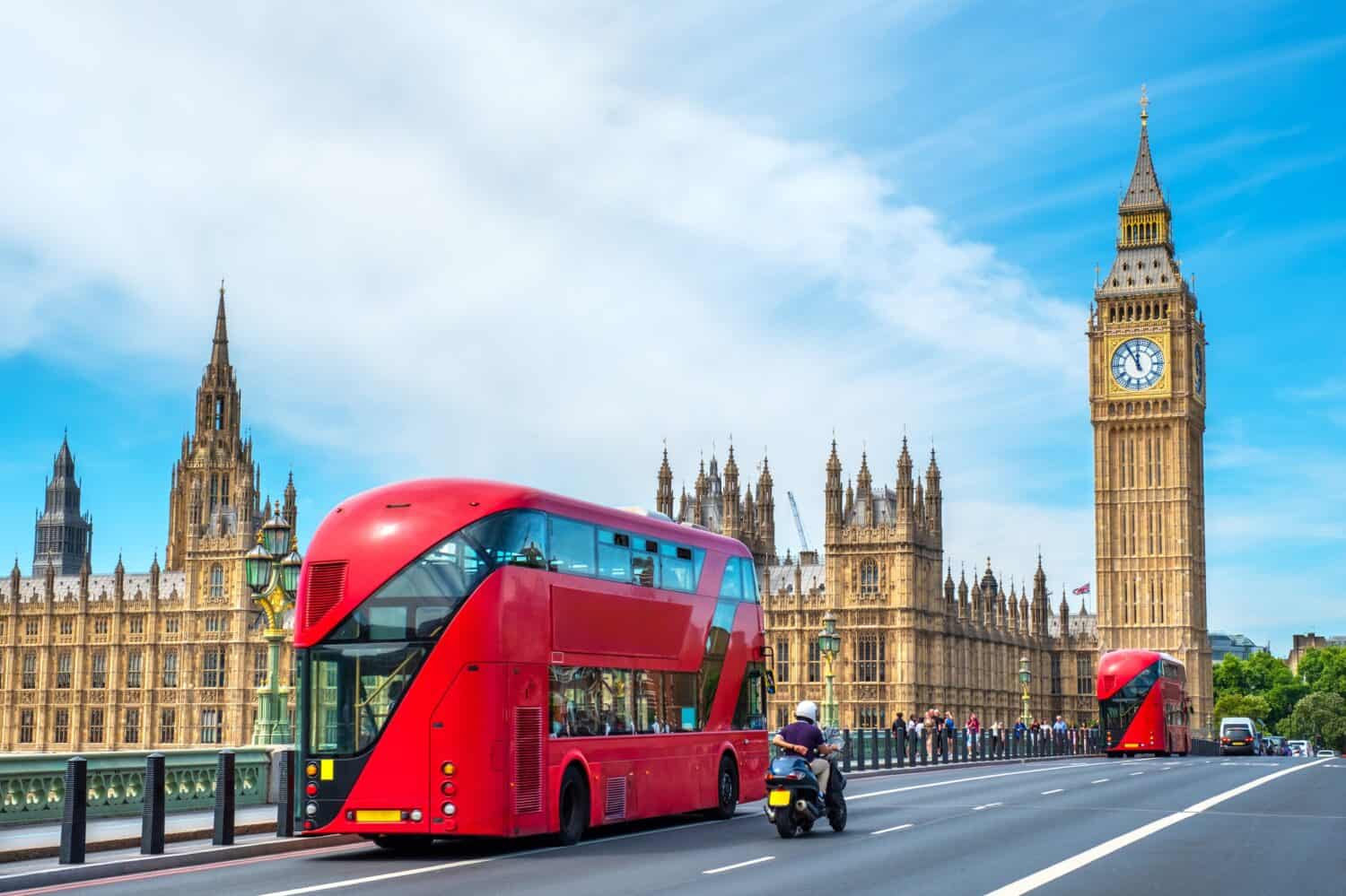 Red double-decker buses pass by Big Ben and the Houses of Parliament on Westminster Bridge. London, England