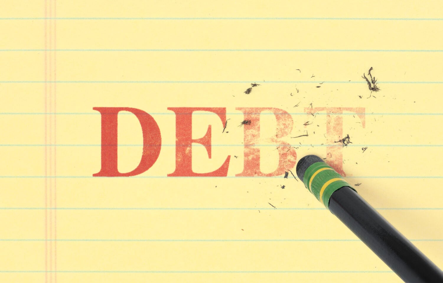 Close up of a black pencil erasing the word, &#039;debt&#039; printed in red on yellow ledger paper.