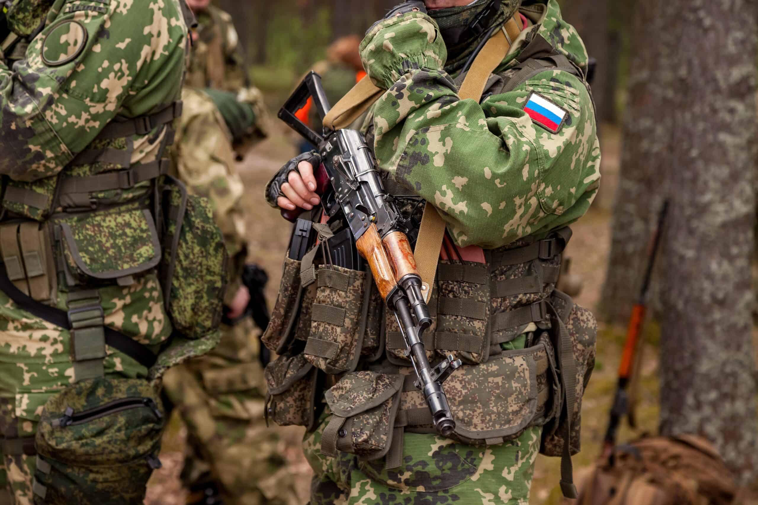 Russia military | Close up hands russian soldier man dressed military camouflage uniform holds weapon in woodland at soldiers background. Male border guard in country border holding machine gun on war. Copy text space