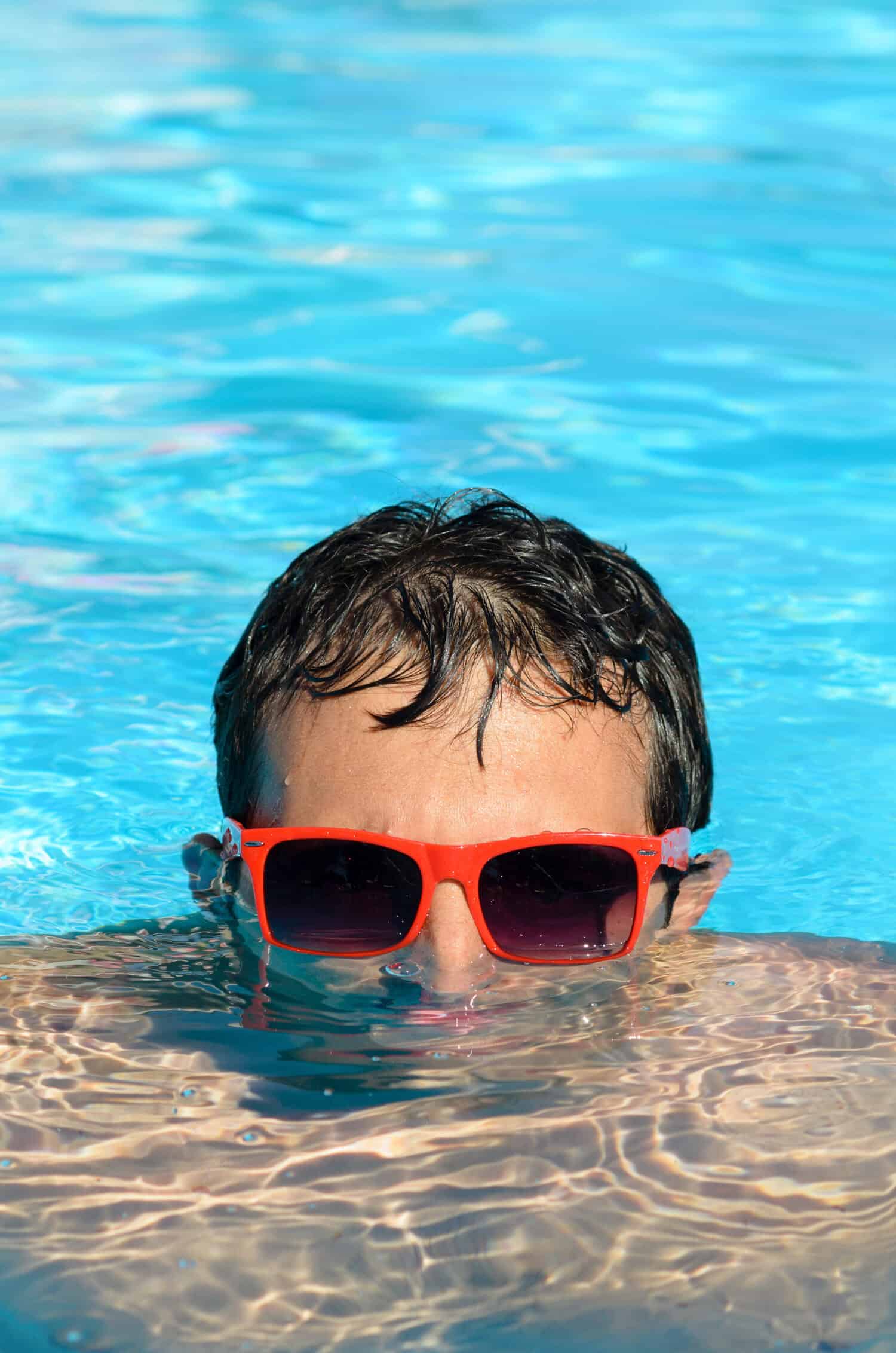 Man in pool having fun on summer holidays. Young man swimming and lurking on vacation. Half head above water stalking.