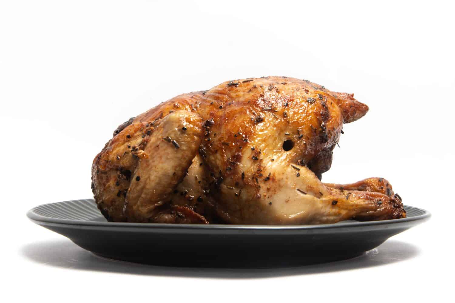 A whole delicious roasted chicken seasoned with herbs in a black plate isolated on white background clipping path