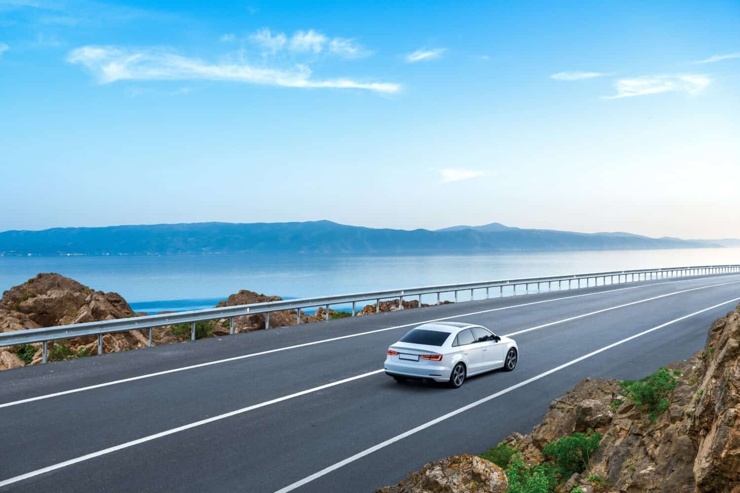White car driving on the coastal road. road landscape in summer. it's nice to drive on beach side highway. Highway view on the coast on the way to summer vacation. Spain trip on beautiful travel road