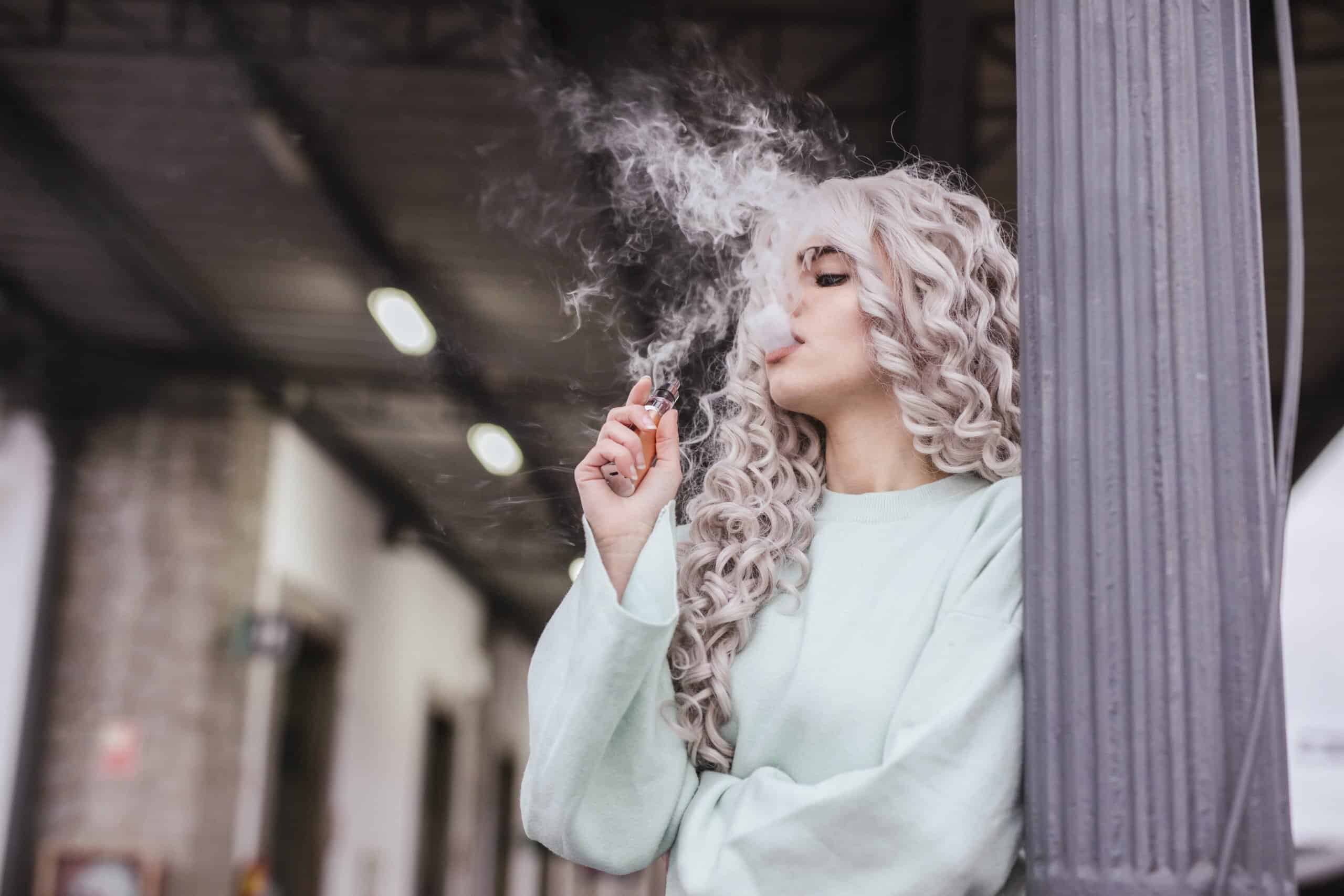 Young woman smoking electronic cigarette on platform