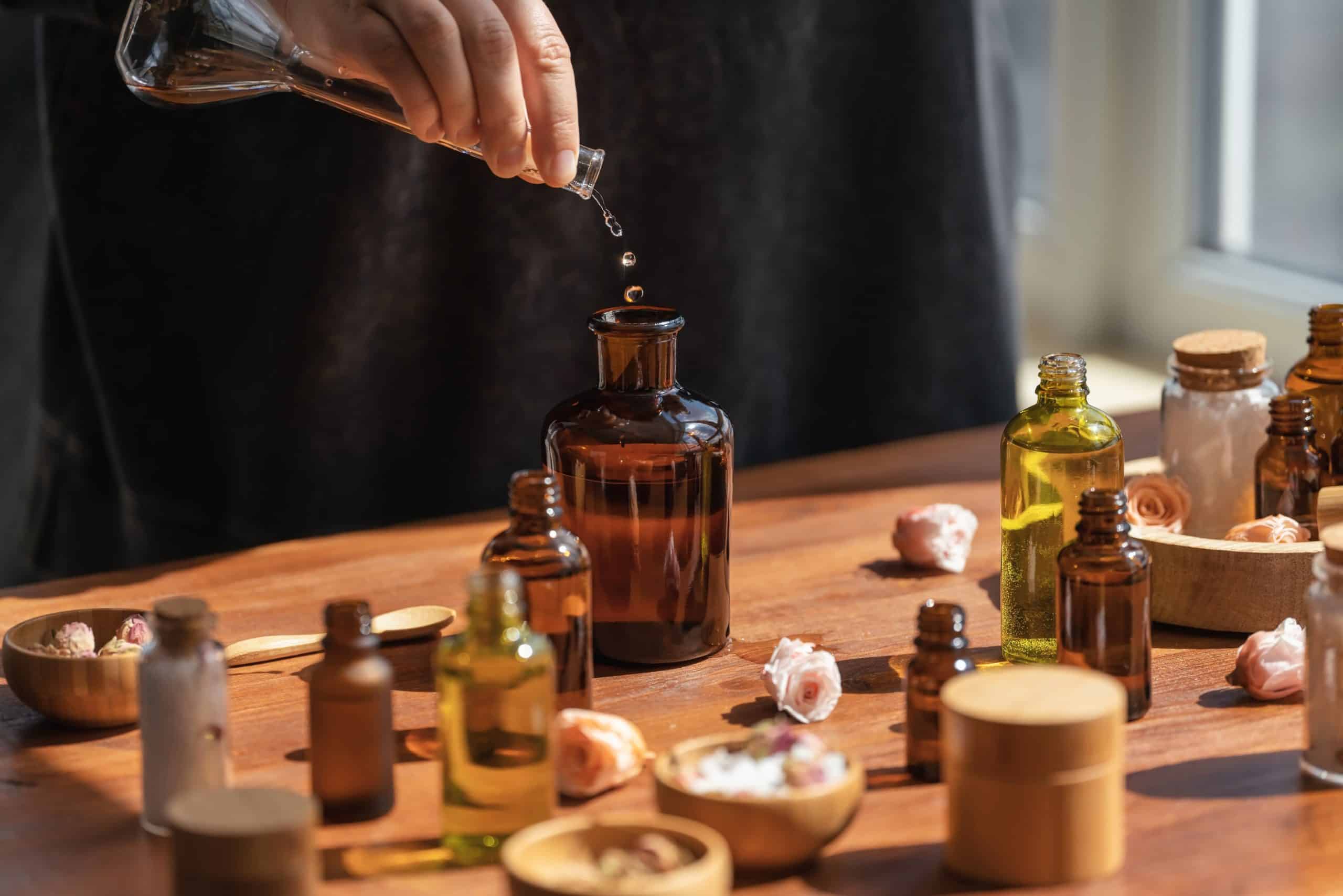 Woman preparing aromatic liquid for diffuser on wooden table. Many bottles and jars with different types of oils, salt and essences. Alternative medicine concept.