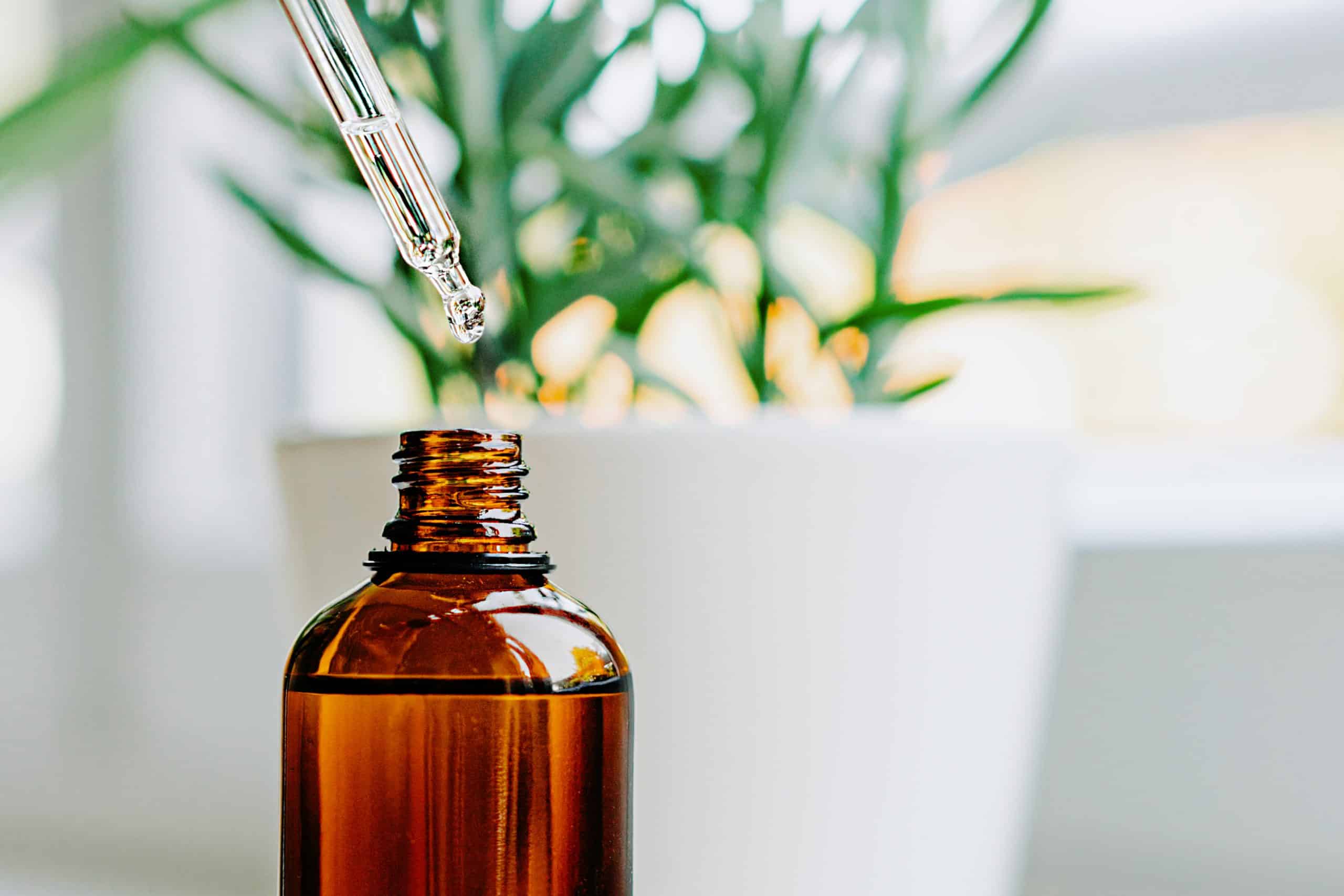 Close up of face serum pouring from a pipette into an amber glass bottle. Natural skincare and essential oil aromatherapy. Health and wellness concept. Copy space.