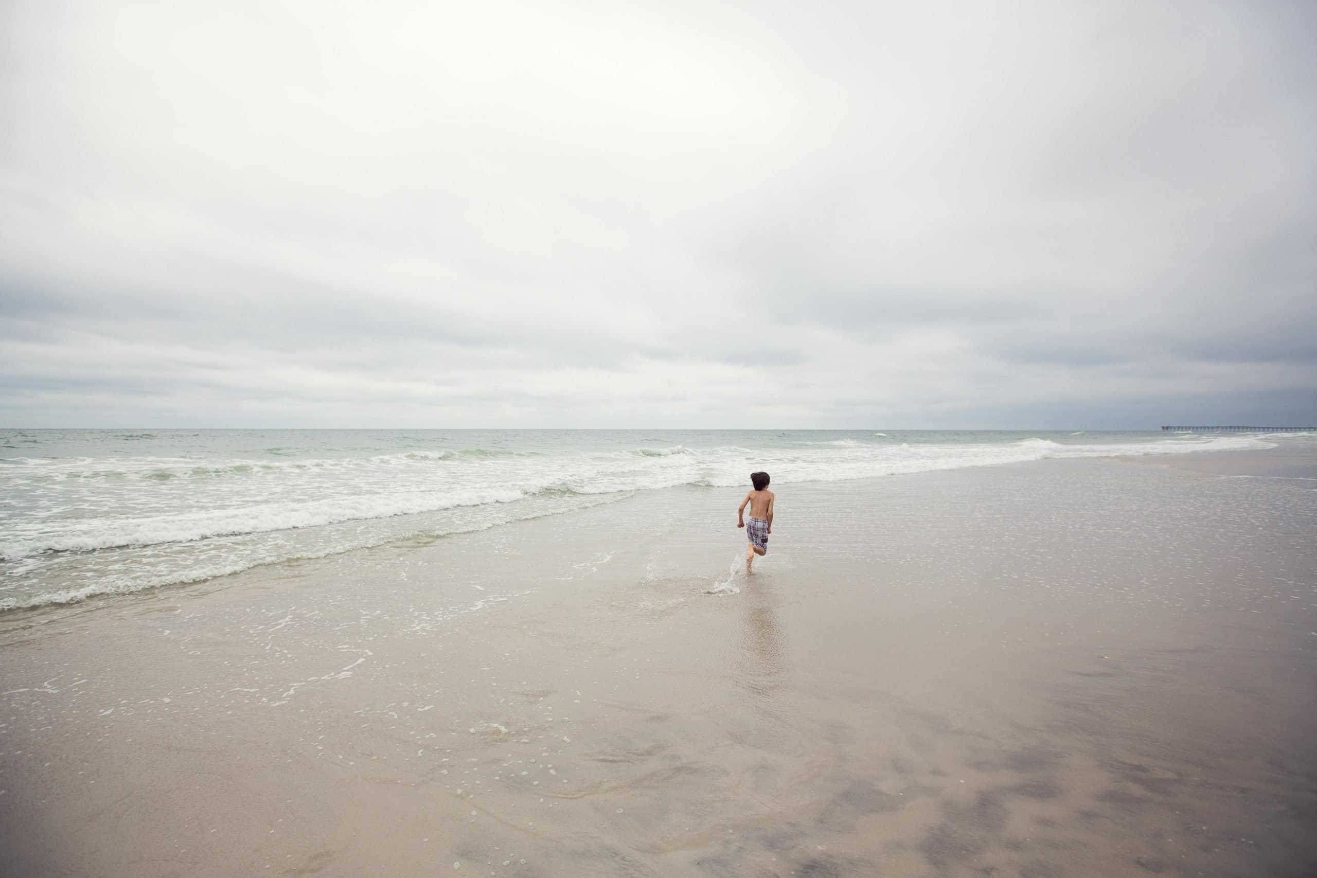 Pender County, North Carolina | USA, North Carolina, Pender County, Topsail Beach, Boy (8-9) running away along beach on overcast day